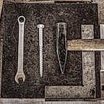 A collection of vintage workshop tools including a wrench, nail, and hammer displayed on a wooden table.